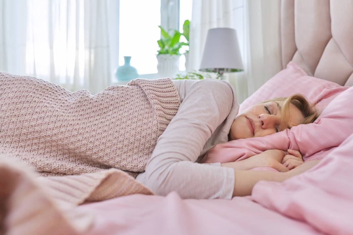 A woman laying in bed upon pink sheets and blankets.