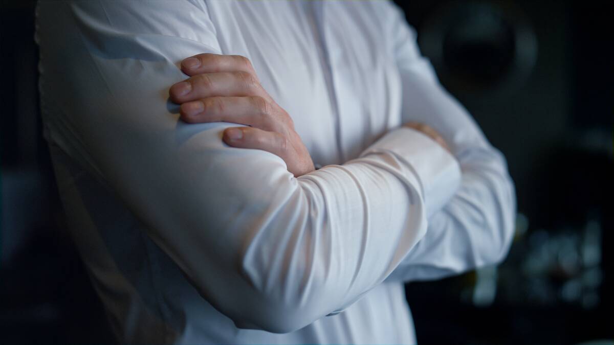 A closeup of a man in a white button up shirt crossing his arms.