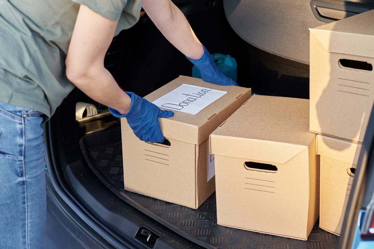 A man loading a box labeled 'donation' into the trunk of a car.