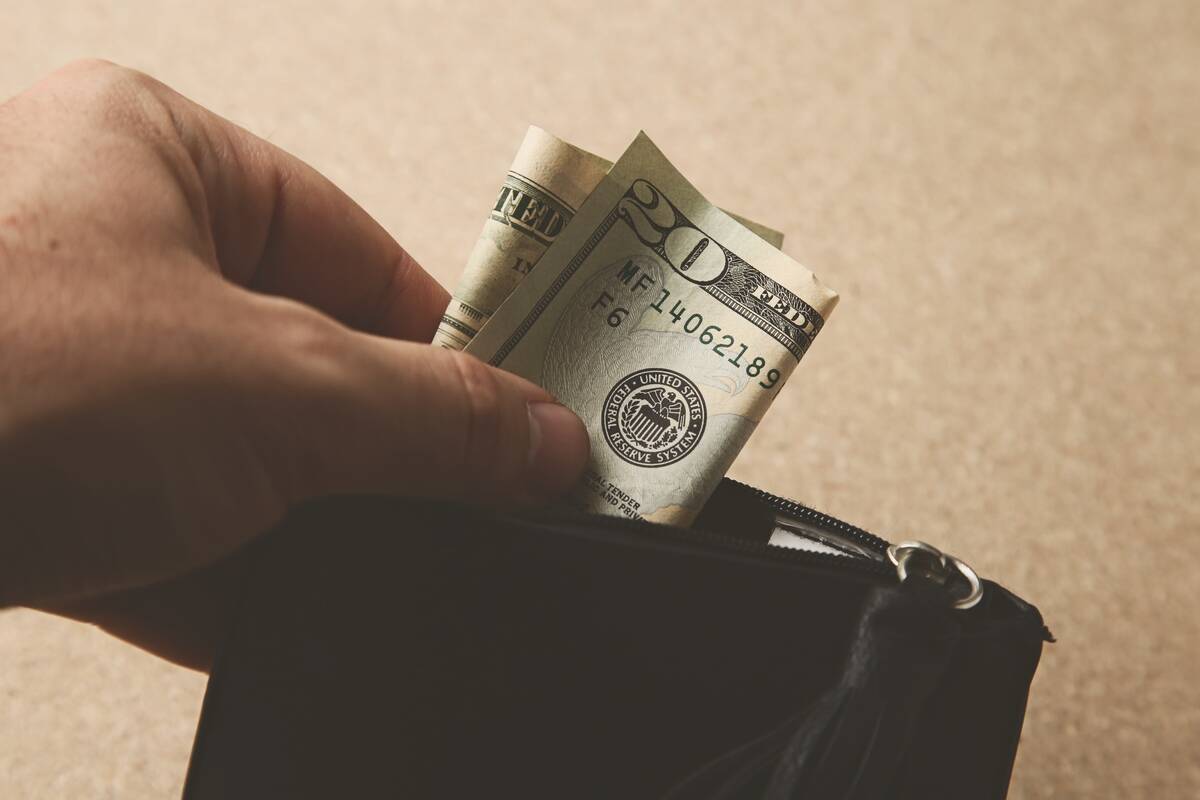 A closeup shot of a person putting some money in his leather wallet.