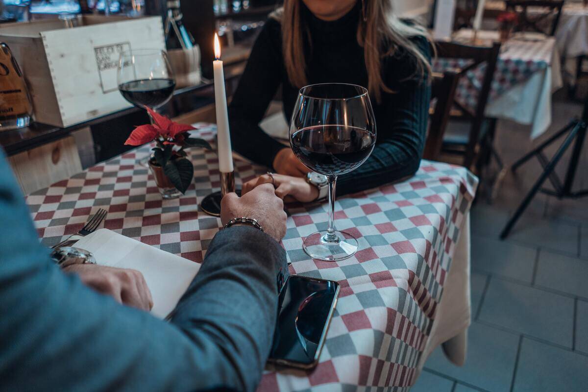 A young couple on a dinner date, holding hands across a table with large wine glasses next to them.