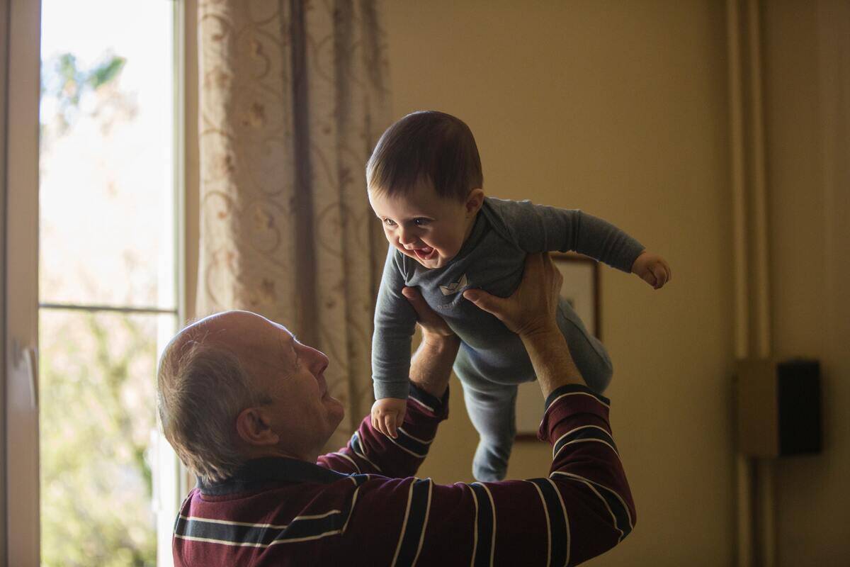 A grandfather holding up his grandson who's smiling and laughing.