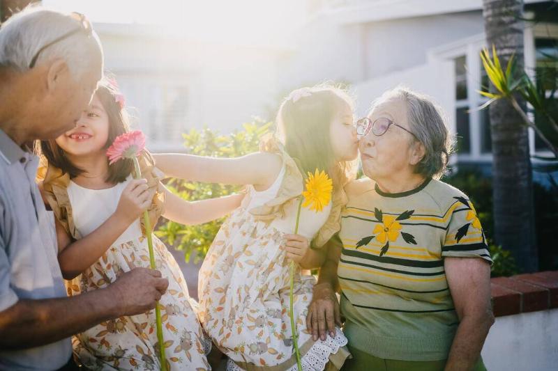 Two grandchildren hanging out with their grandparents, holding flowers and kidding their grandma on the cheek.