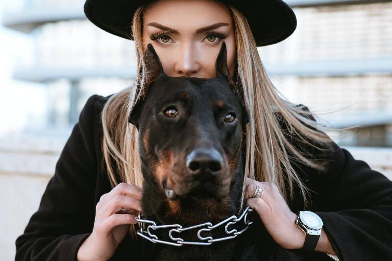 A woman half crouched behind her dog, a doberman in a chain collar.