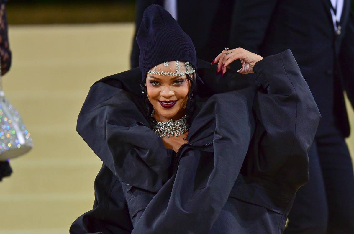 Rihanna arrives to the 2021 Met Gala Celebrating In America: A Lexicon Of Fashion at Metropolitan Museum of Art on September 13, 2021 in New York City. She's in a large, puffy black dress, a tall, slouched black hat, and crystal jewelry on her forehead and neck.