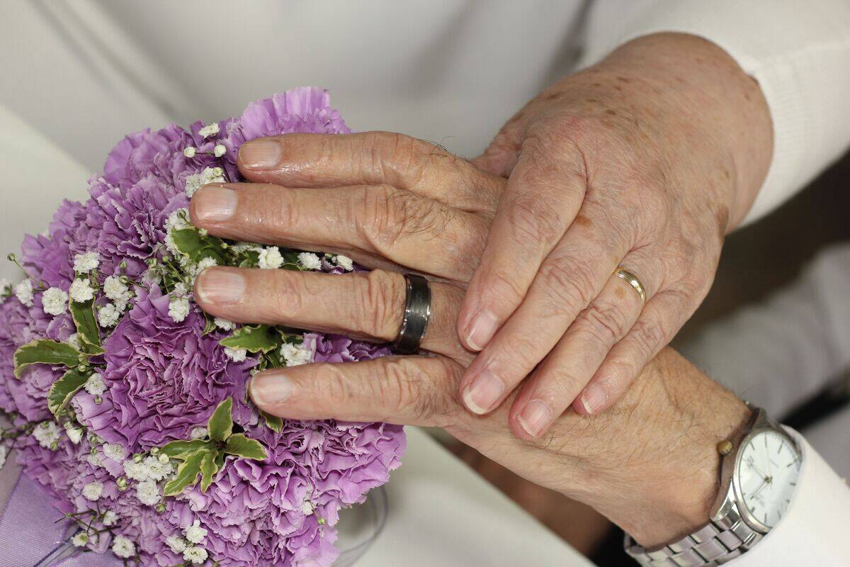 Elderly couple holding hands and showing their wedding rings and bouquet