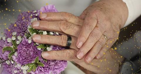 Elderly couple holding hands and showing their wedding rings and bouquet, constellations decorating the corners of the image.