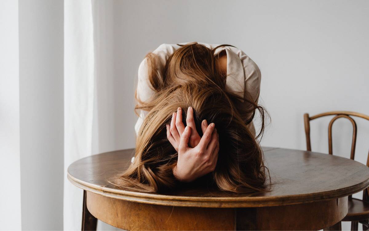 A woman leaning forward on a table, head in her hands, appearing frustrated.