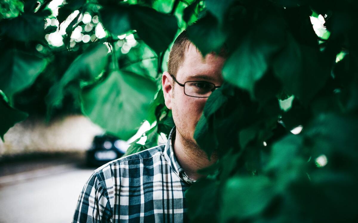 A man half-hidden among the leaves of a bush.