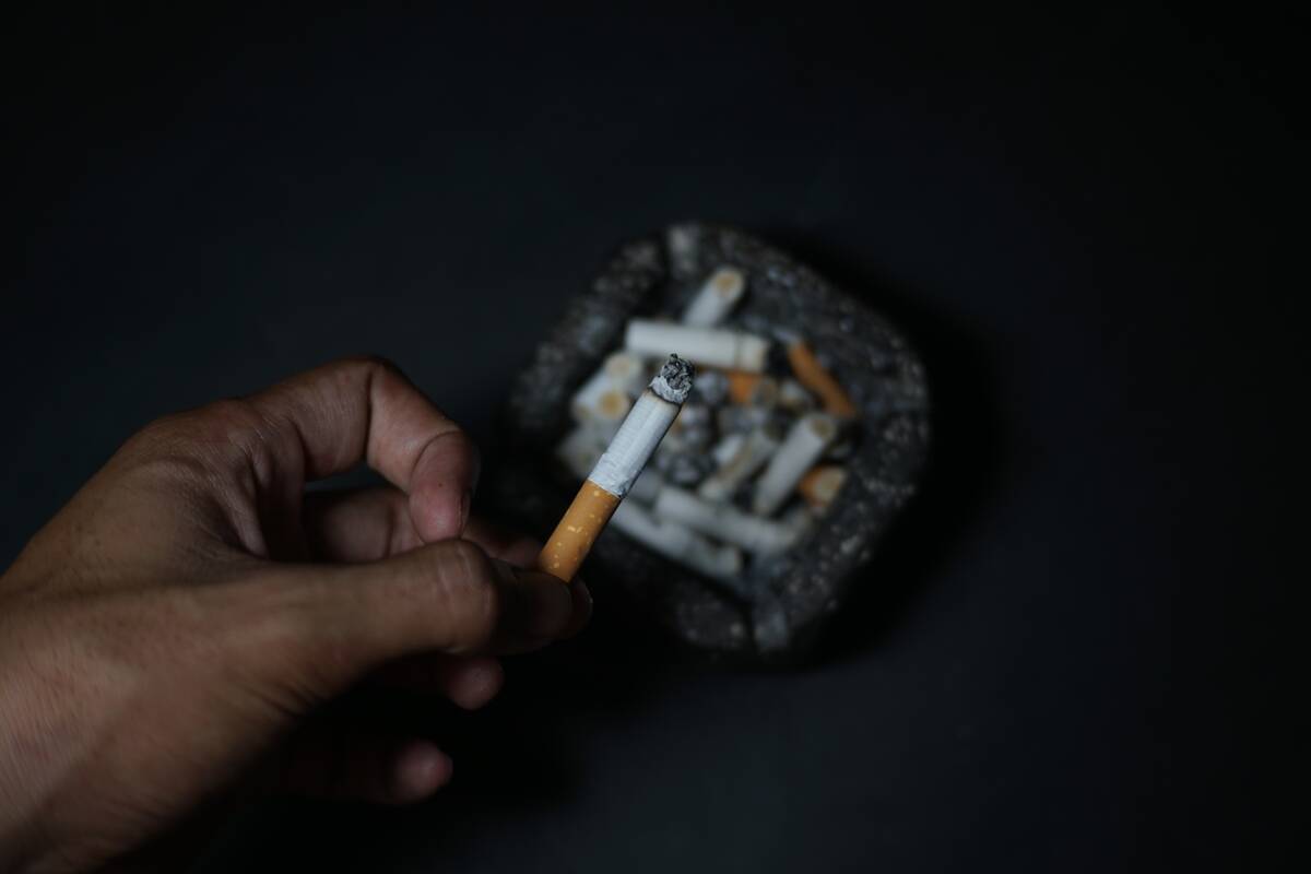 Someone holding a half-finished cigarette over an ash tray.