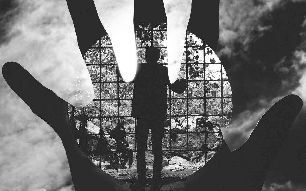 A man looking out through a large, circular grate with the negative overlay of a hand on top.