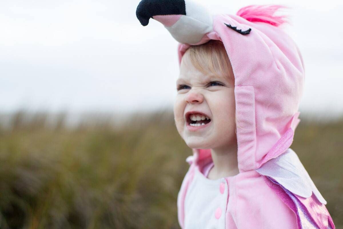 A little girl in a flamingo onesie making an angry face.