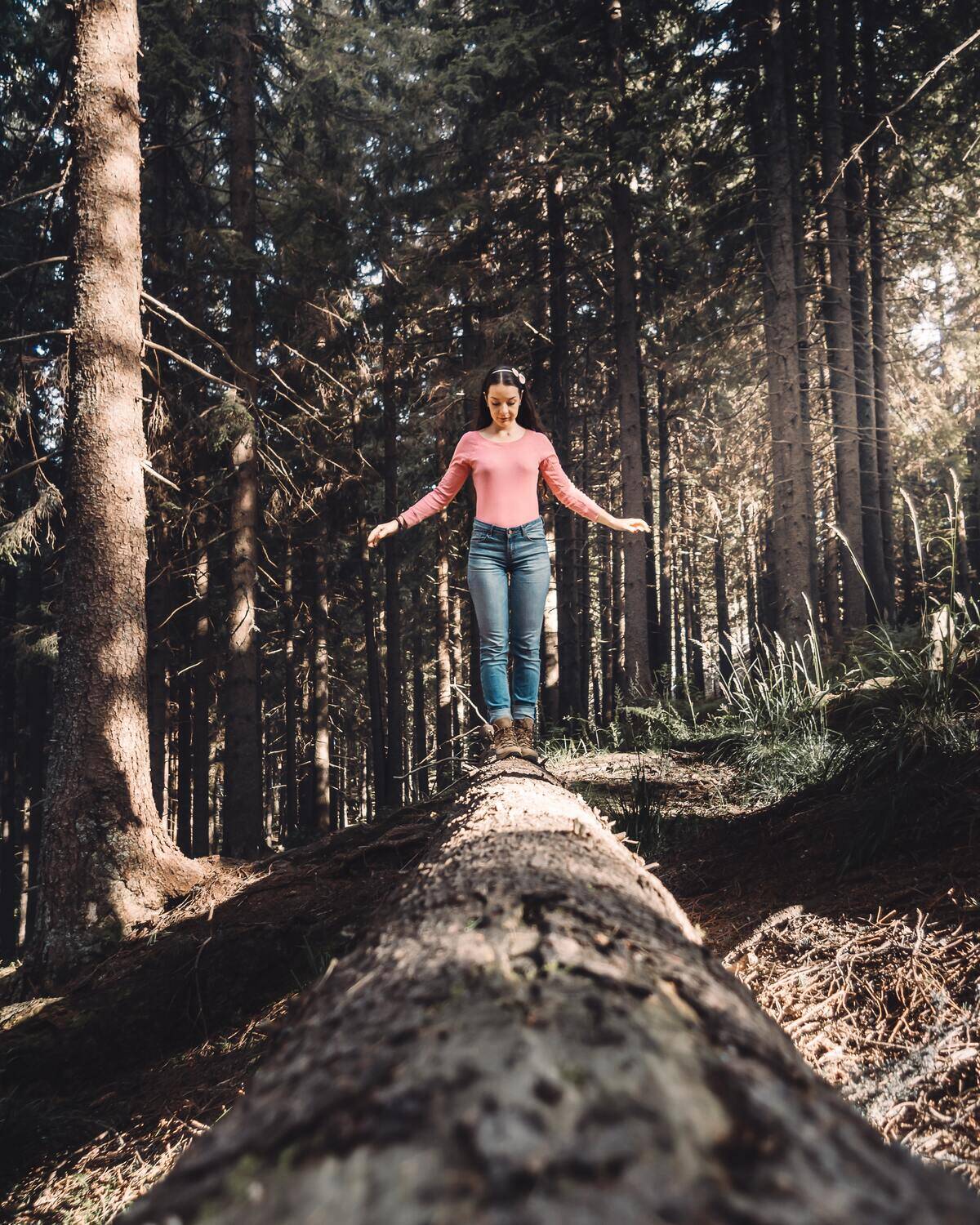 A woman walking along the trunk of a fallen tree in a forest.
