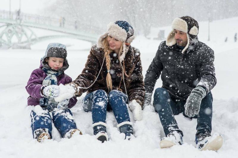 Two parents and their daughter sitting in the snow, the mom helping the daughter make something.