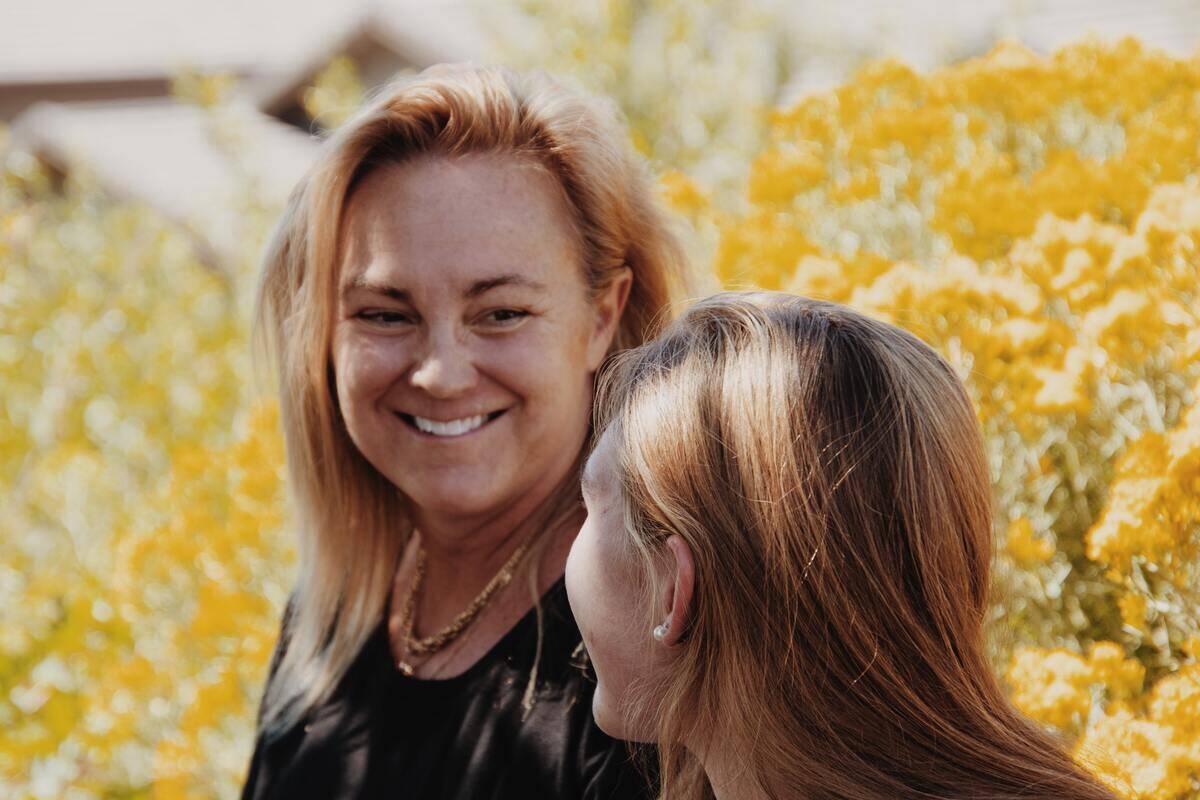 A woman smiling at her friend as they walk among some yellow flowers.