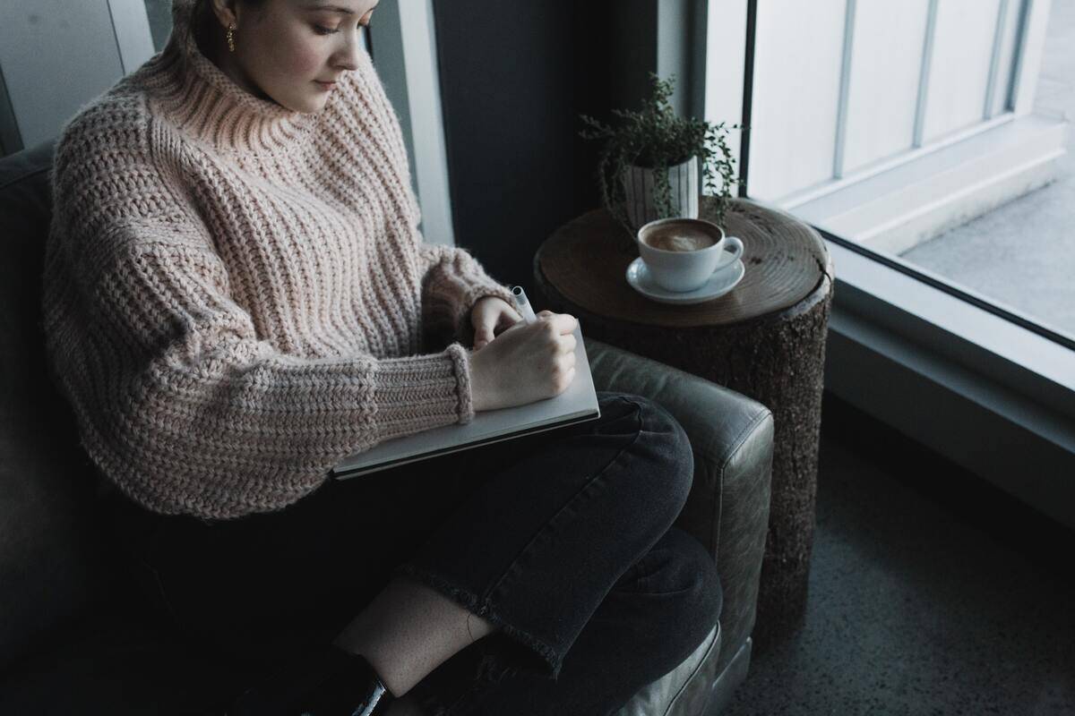 A woman curled up in a chair writing in a journal.