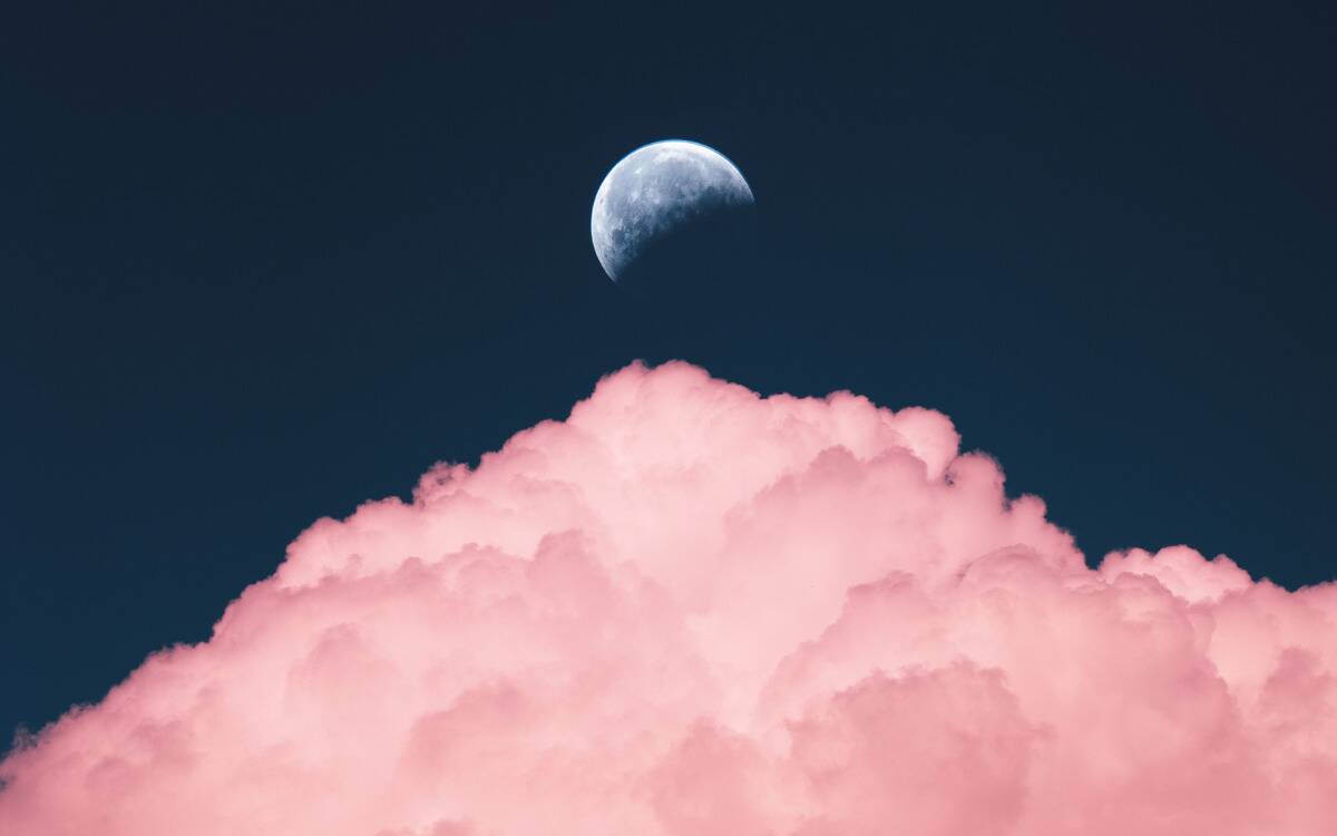 The moon in the sky above a large, pink lit cloud.