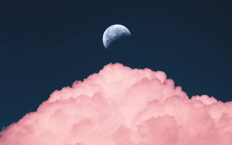 The moon in the sky above a large, pink lit cloud.