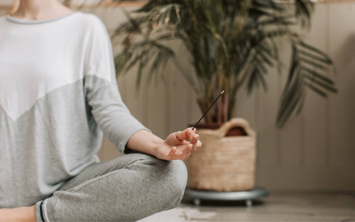 A woman meditating, holding an incense stick in her hand.