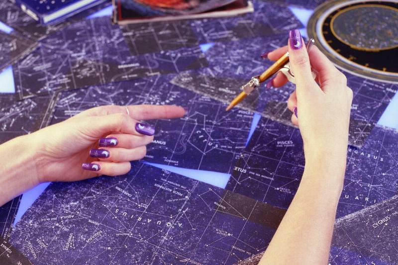 A woman pointing and drawing atop constellation maps.