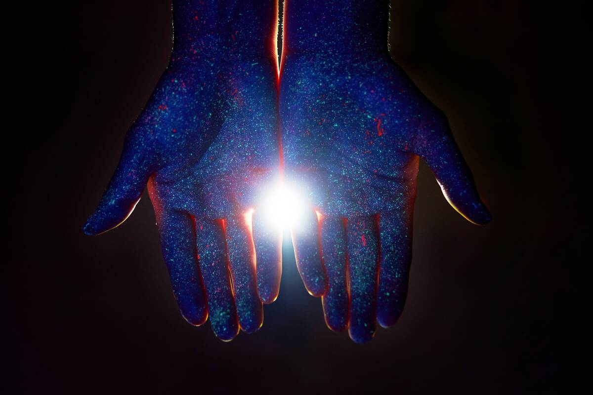 Light through the palms of two hands overlaid with a speckled galaxy pattern.