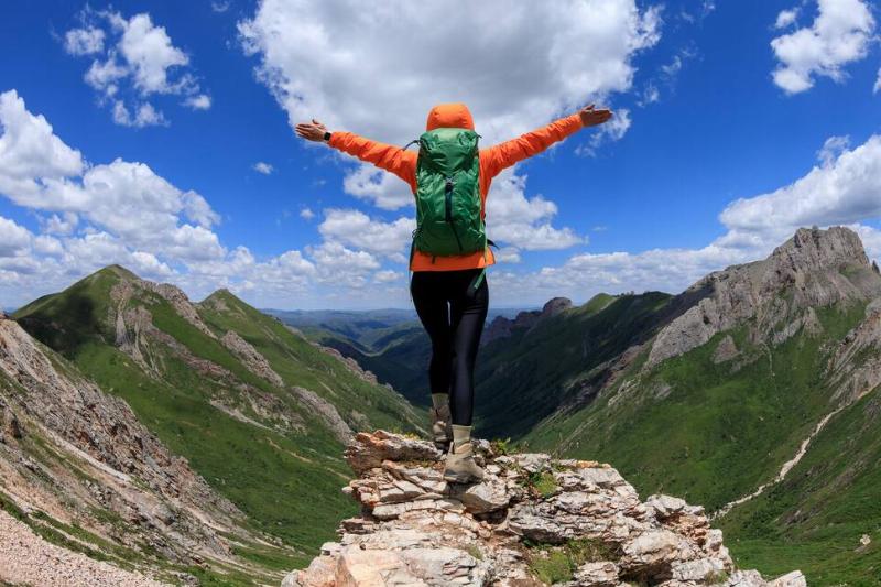 Successful woman backpacker hiking on alpine mountain peak, arms outstretched as she stands upon a peak.