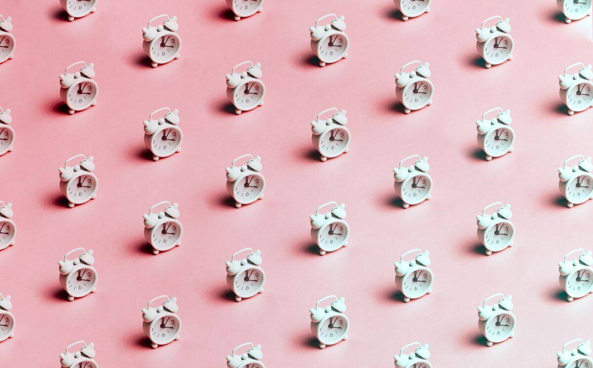 Rows of identical alarm clocks against a pink background.