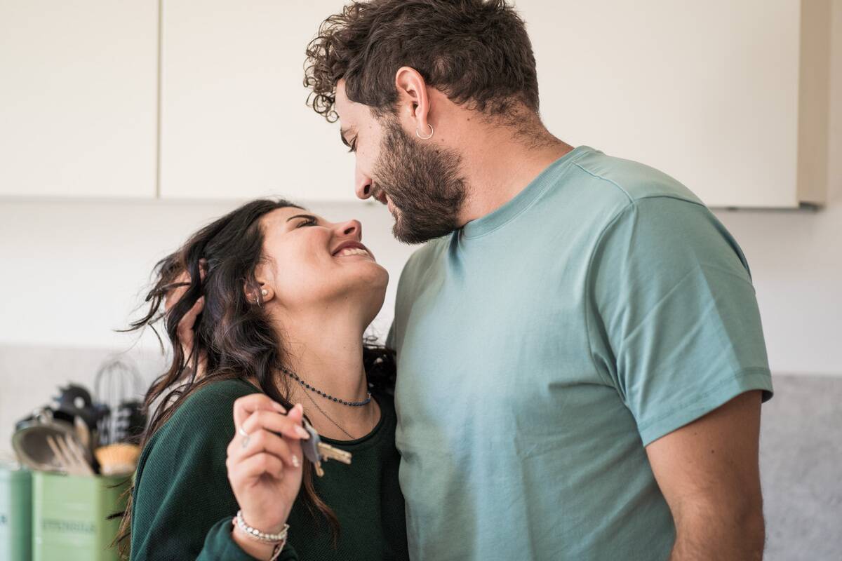 A young married couple rejoices over the purchase of the new house - the two newlywed young people look into each other's eyes and hold the keys to the apartment.