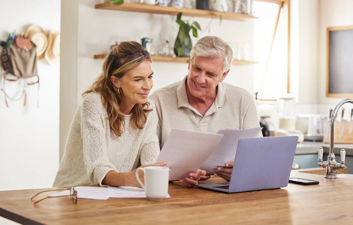 A couple sitting, looking at a laptop and some documents together.