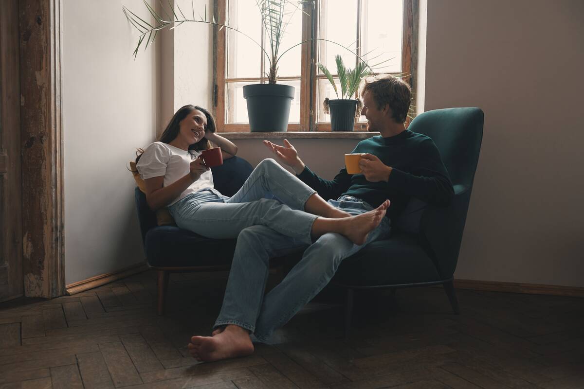 Happy young couple enjoying hot drinks and talking while relaxing at home together