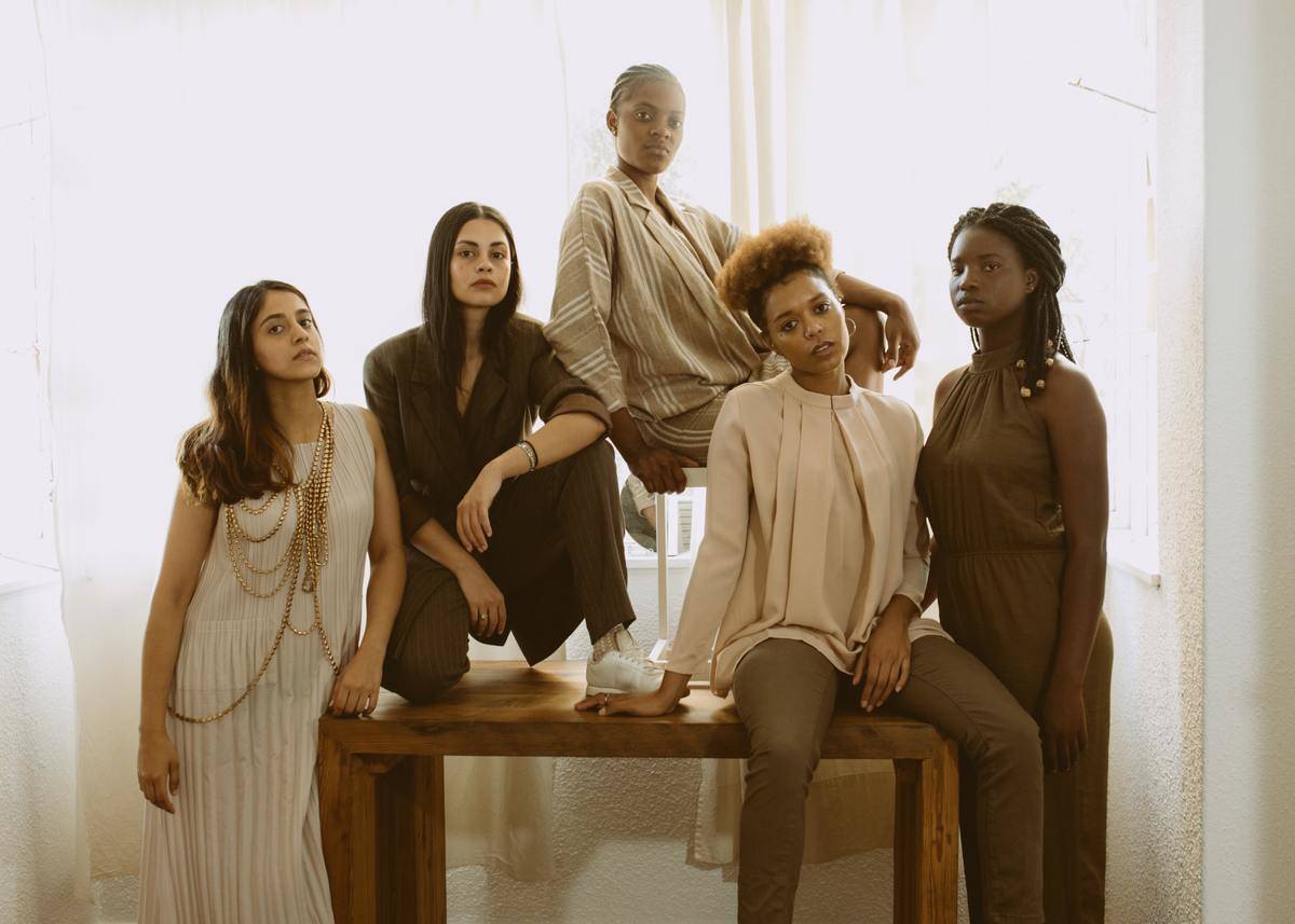 A group of women, all dressed in earth tones, posed around a table, looking at the camera.