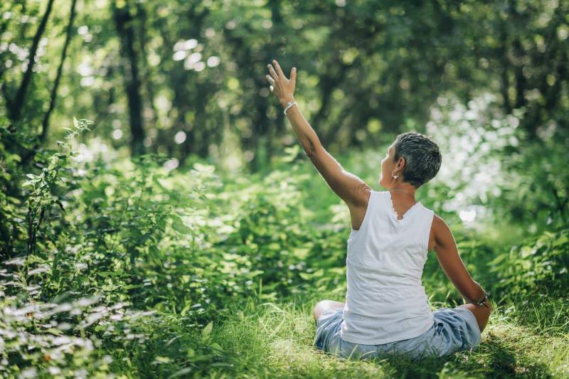 A mindful woman meditating, surrounded by beautiful nature, reaching up and to her left.