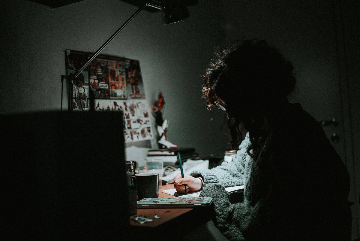 A woman seated at a desk in the dark, taking notes.