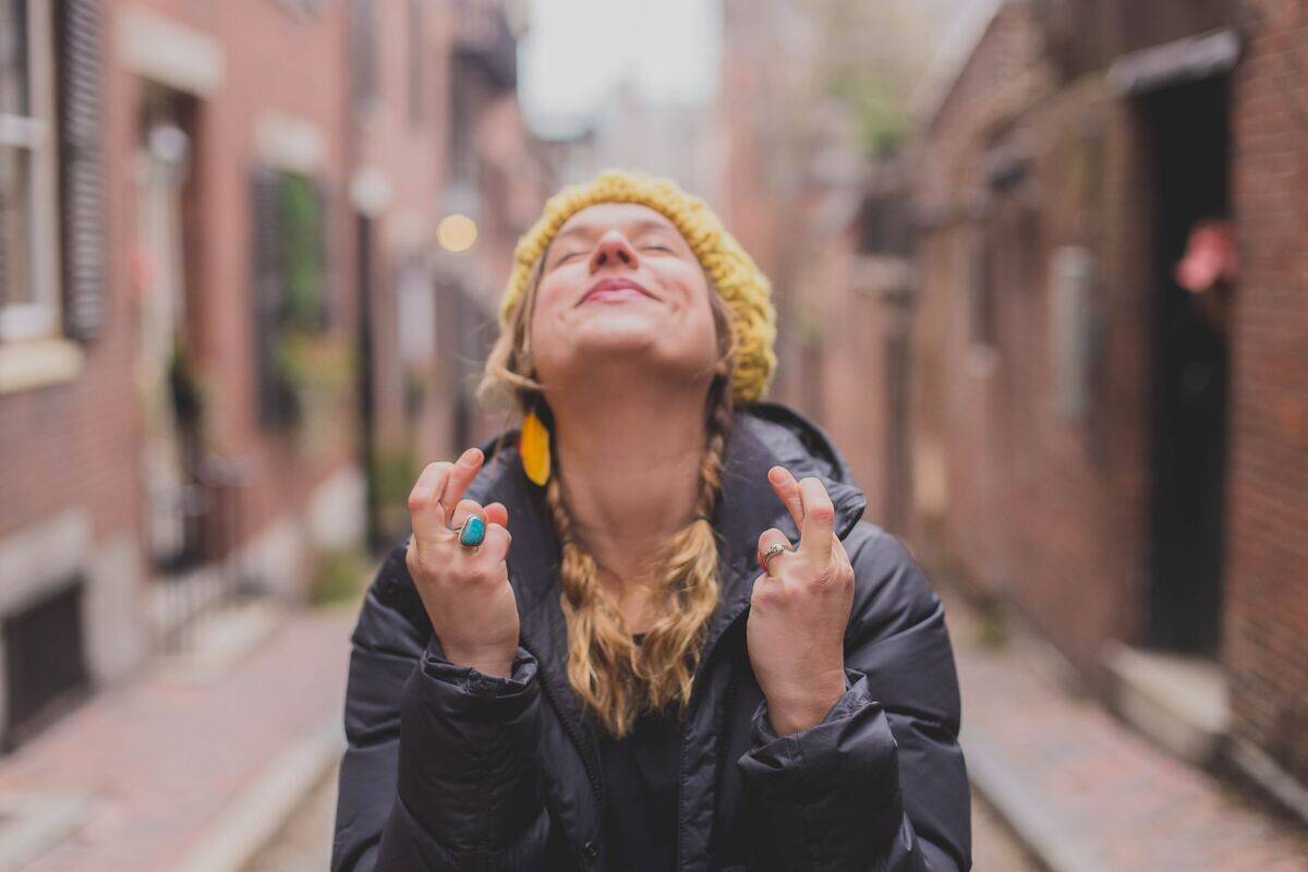 A woman looking upwards, eyes closed, fingers crossed on both hands.