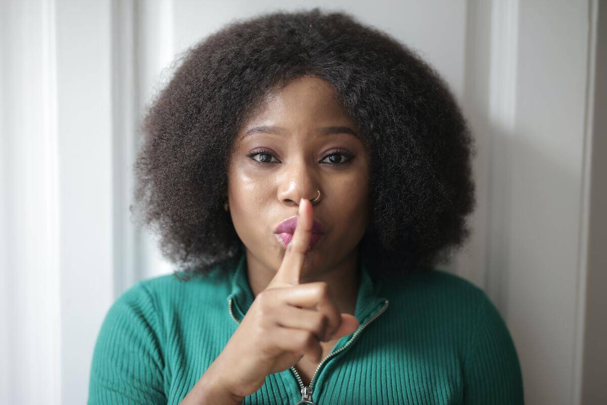 A woman looking directly at the camera, a finger over her mouth.