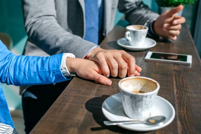Couple of coworkers holding hands during coffee break