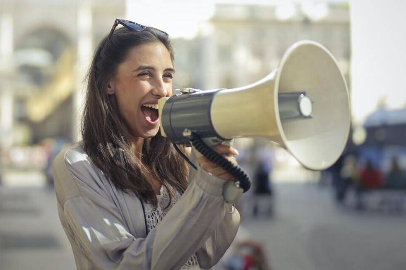 A woman speaking excitedly into a megaphone out on the street.