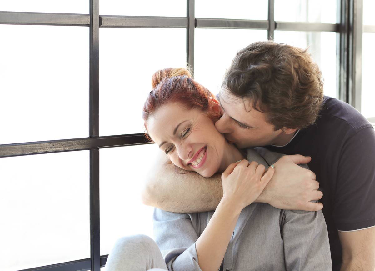 A couple embracing and kissing in front of a window.