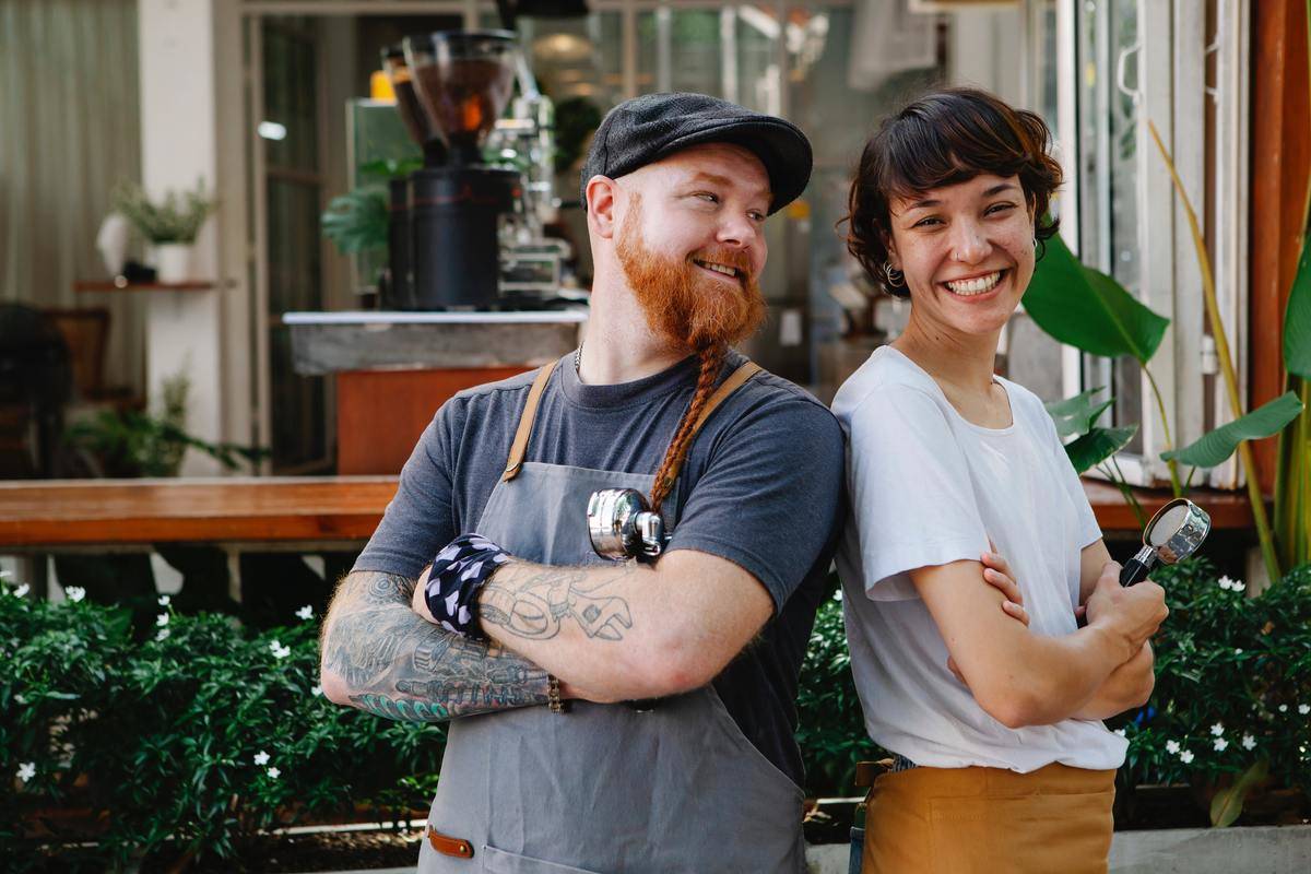 Two coffee shop coworkers standing back to back, arms folded, smiling.