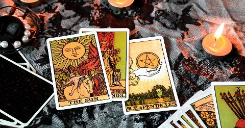 Three tarot cards (The Sun, the Queen of Wands, and the Ace of Pentacles) laid our on a grey and black tablecloth surrounded by tea lights.