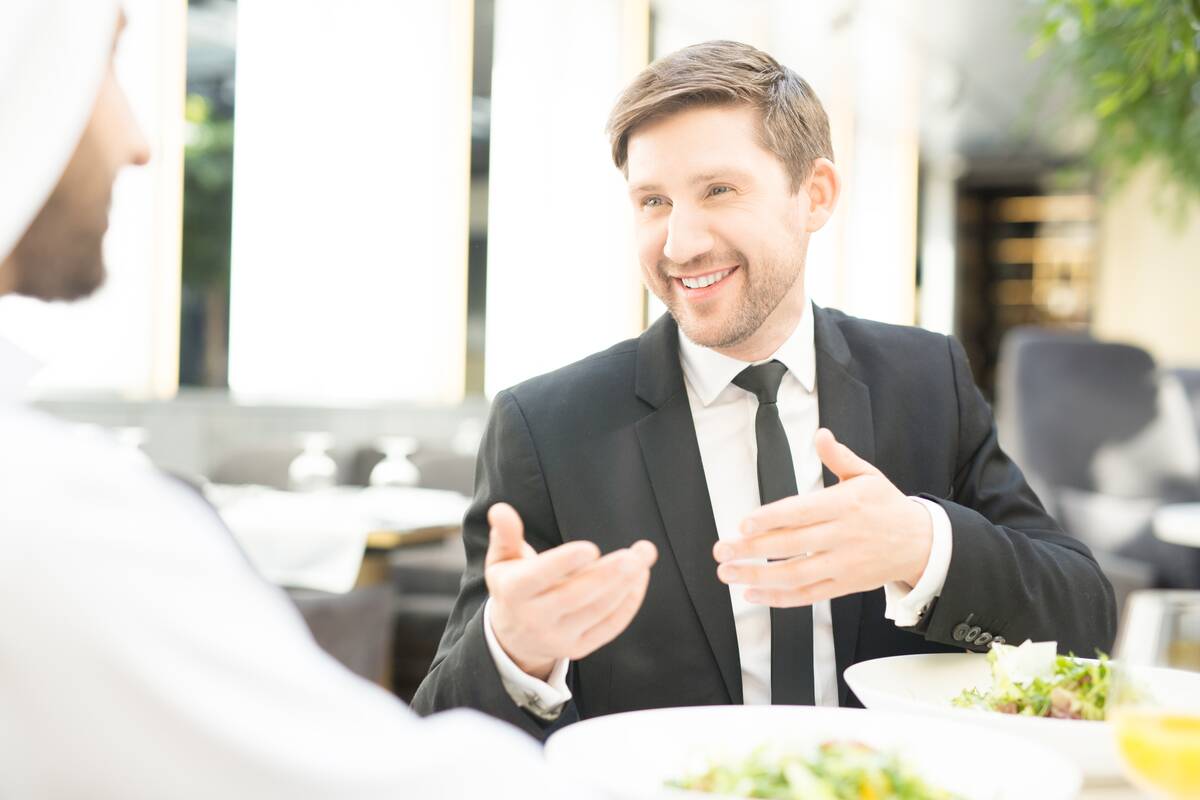 Young smiling businessman in suit having talk to his foreign guest during business lunch in restaurant