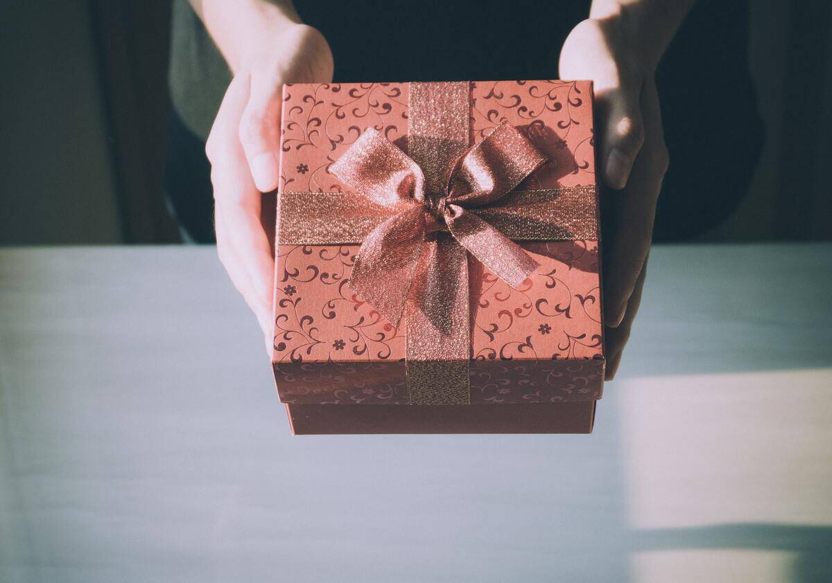 Someone holding a red gift box, complete with a bow, as if they're handing it forward.