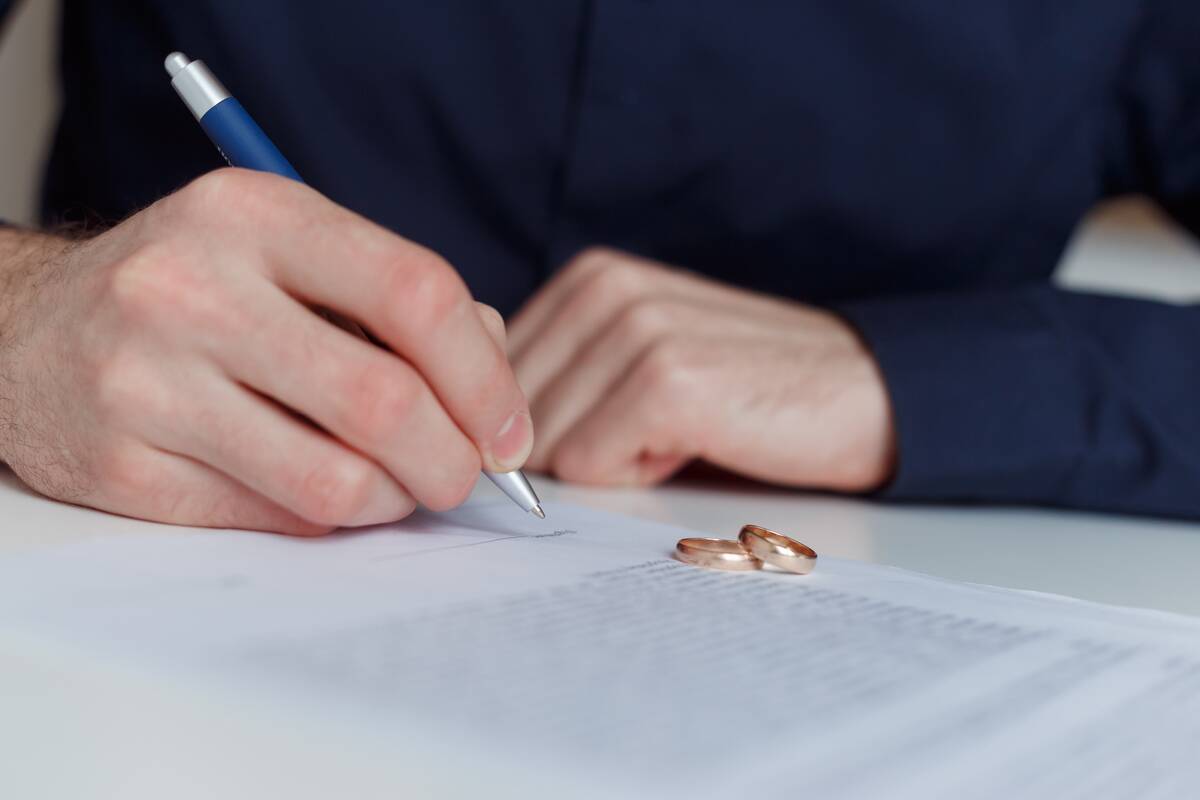 Husband signing divorce agreement with both wedding rings on the table.