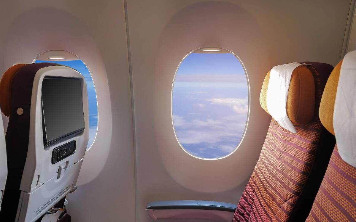 A seat inside a plane next to a window that shows the blut sky.