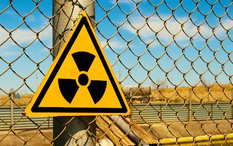 A triangular radiation sign on top of a chain link fence.