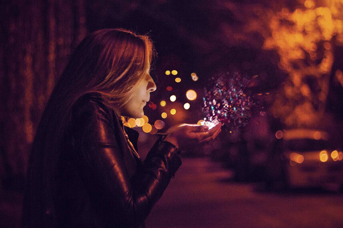 A woman blowing on a handful of confetti as if making a wish, standing in the street.