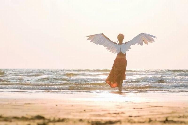 Woman standing on a beach with her arms outstretched, wearing angel wings.