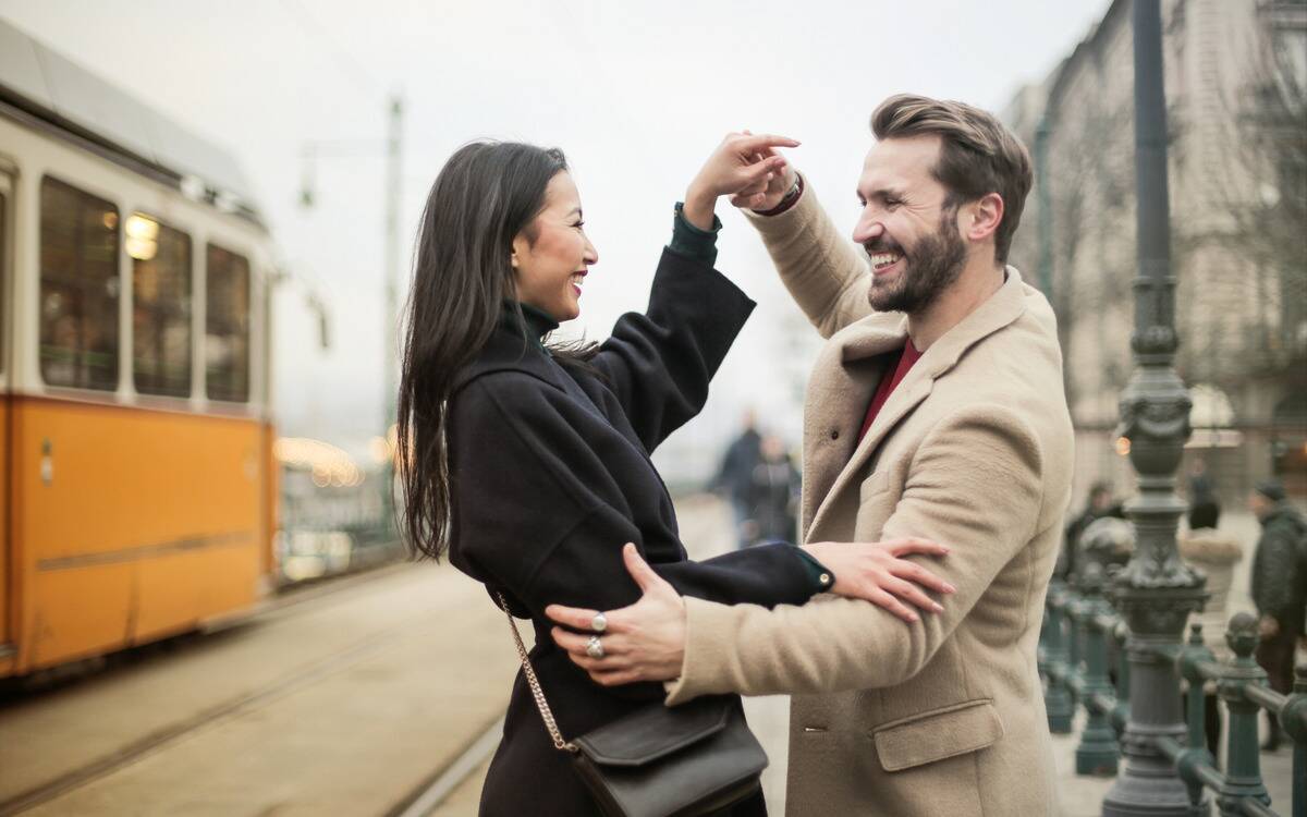 A couple smiling as they dance on the street.
