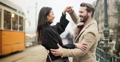 A couple smiling as they dance on the street.