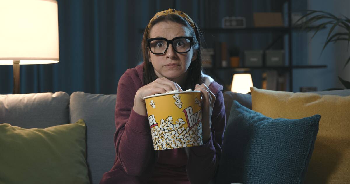 Woman watching a scary movie at home alone and eating popcorn.